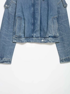 Detailed close-up of light blue washed denim jacket with metal button and large side pockets