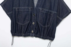 Detail of dark blue denim top with white contrast stitching, chest pockets and metal buttons