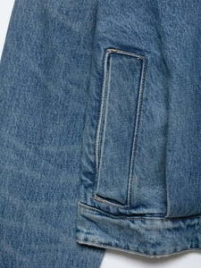 Detail view of blue denim jacket showing rectangular patch pocket with yellow stitching