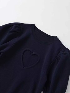 Detail of navy knit top featuring puff sleeves and textured heart pattern on the front