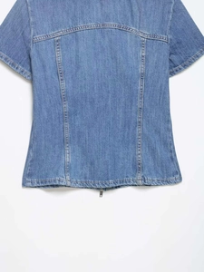 Detail view of denim top back featuring structured seams and metal zipper at the bottom hem