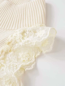 Close-up of cream knit fabric with delicate layered floral lace edge and ribbed texture