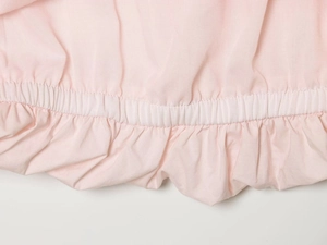 Detail of light pink mini dress showing elastic hem and textured woven fabric ruffles
