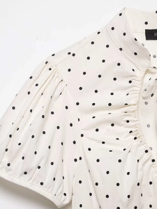 Close-up of beige puff sleeve shirt with black polka dots and ruffle collar details