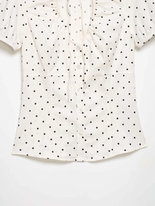 Detail of ruffled V-neckline and transparent buttons on polka dot puff sleeve shirt