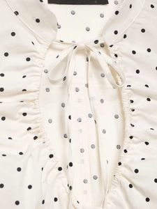 Detail of white black polka dot blouse showing ruffled neckline and drawstring bowtie