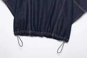 Detail of dark blue denim hem with contrast white stitching and elastic drawstring toggle