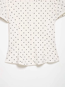 Detail view of white polka dot short sleeve shirt with ruffled edges and lightweight fabric