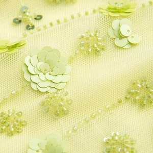 Détail du tissu en maille jaune clair avec fleurs en paillettes 3D et perles fait main