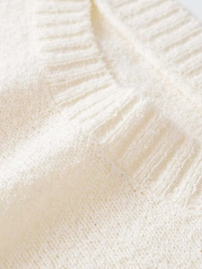 Macro shot of cream white knit fabric with soft textured yarn and ribbed stitch detail