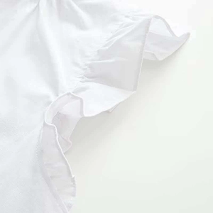 Close-up detail of white blouse featuring delicate ruffles and breathable cotton texture