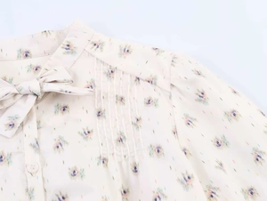 Detail of floral chiffon shirt featuring bow tie neckline and elegant vertical pleats