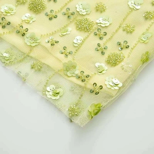 Gros plan sur tissu en tulle vert clair avec fleurs à paillettes 3D et perles artisanales