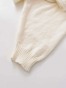Close-up of the ribbed cuff detail on an elegant cream-white long-sleeve knit sweater