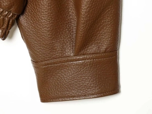 Detail view of brown faux leather jacket cuff with elastic hem and fine stitching