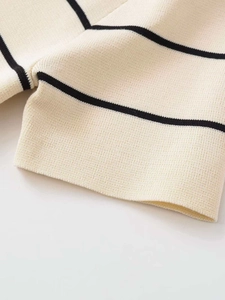 Dettaglio dei polsini in maglia bianco crema con strisce nere e bottoni dorati fini