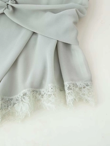 Dettaglio del top in georgette verde chiaro con delicato bordo in pizzo bianco sull'orlo
