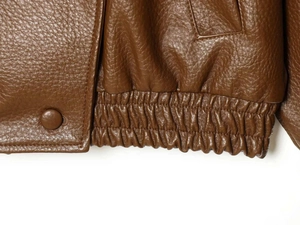 Detailed macro view of the brown PU leather jacket featuring elastic hem and snap button