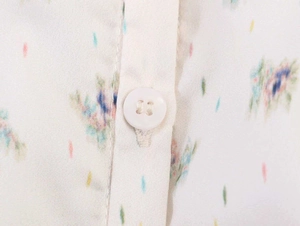 Macro detail of white floral print shirt showing fabric texture and resin button closure