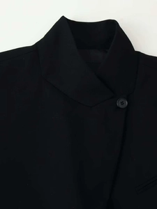 Détail du revers d'un blazer noir montrant la texture du tissu et un bouton unique
