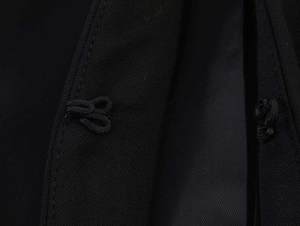 Close-up of black irregular suit set showing traditional frog button and twill texture