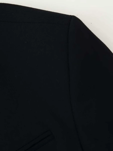 Détail macro de la couture d'épaule et texture tissée sur un blazer noir à col montant