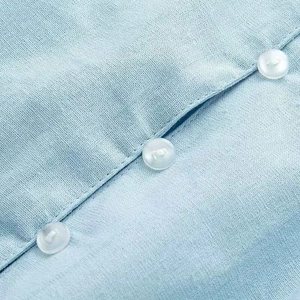 Close-up of three white buttons on a light blue linen shirt with visible woven texture