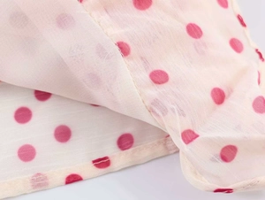 Close-up of pink polka dots on beige georgette fabric with fine vertical stripe texture