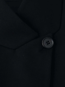 Gros plan du col de blazer noir avec texture sergée et détails sur le bouton à quatre trous