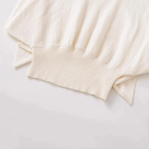 Close-up of beige knit sweater showing detailed ribbed cuff and soft textured fabric