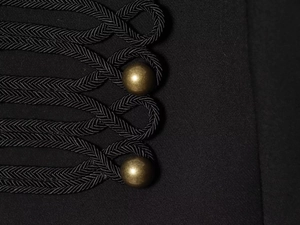 Detailed macro view of black military style braided frog closures and bronze metal buttons