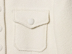 Détail macro de la veste bouclée blanc cassé avec bouton recouvert de tissu et poche
