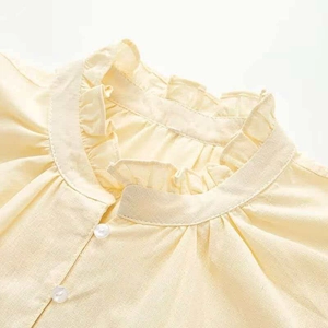 Close-up of frill standing collar and pearl buttons on a light yellow summer shirt