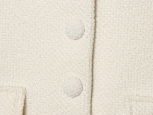Vue détaillée de la texture bouclée crème et des boutons recouverts de tissu sur la veste