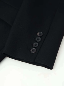 Détail de la manche d'un blazer noir avec quatre boutons et texture de tissu en sergé