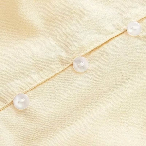 Detail of white buttons and linen fabric texture on a light yellow summer shirt