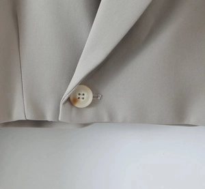 Detailed view of taupe blazer with notched lapel and textured four-hole button