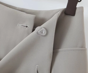 Detail view of grey suit trousers waist featuring a clear button and fine fabric texture