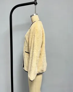 Détail d'un manteau en fausse fourrure beige avec bordures noires et boutons contrastés