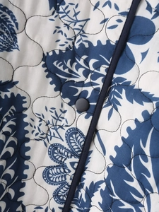 Detail of floral printed quilted jacket featuring blue botanical patterns and a snap button