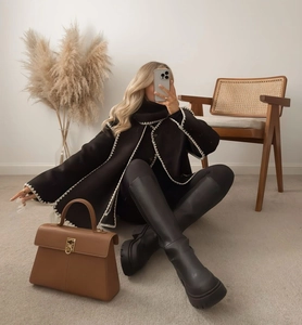 Close-up of black cape coat with white wave trim and chic leather handbag detail
