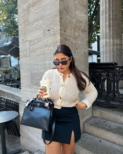 Close-up of white bouclé knit cardigan with gold buttons and black slit skirt outfit
