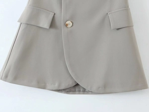Close-up of grey blazer skirt hem featuring curved overlap design and amber button