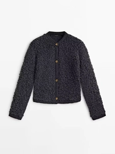 Detailed close-up of dark grey boucle knit fabric with vintage gold buttons on jacket