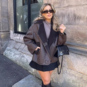 Brown oversized shearling jacket styled with a black pleated skirt and tall leather boots