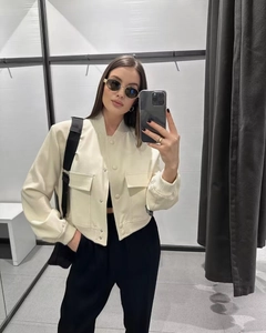Detail of a cropped cream aviator jacket featuring large front pockets and button closure