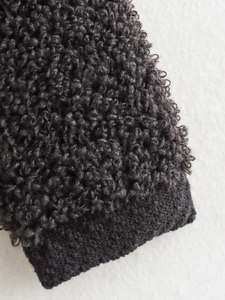Detail of dark grey boucle knit cardigan showing textured fabric and ribbed cuff detail