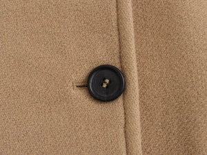 Macro shot of matte black button and neat stitching on camel wool blend coat fabric