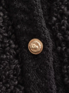 Detail of a gold lion head relief button on thick black teddy fleece knit fabric