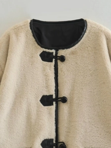 Détail d'un manteau en fausse fourrure crème avec garniture en cuir et fermoir brandebourg